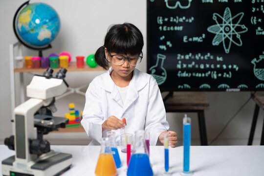 Asian girl scientist carefully examining beaker with blue liquid, showing focus, learning, and excitement in science exploration.