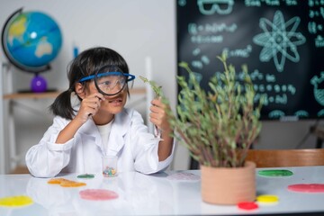 Wearing safety goggles, a young scientist uses a magnifying glass to closely study a leaf specimen in a test tube, demonstrating careful observation skills in biology.