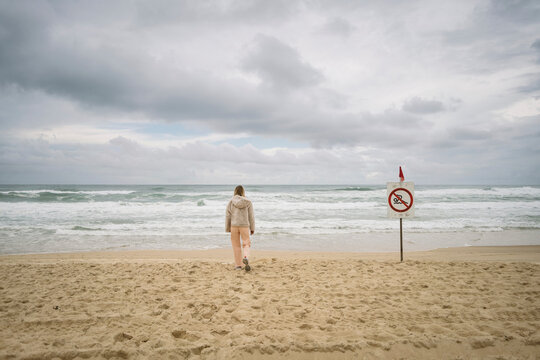 Woman standing on a sandy beach near ocean with no swimming sign