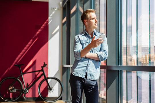Business employee with smartphone by glass window in office - Powered by Adobe
