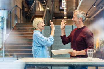 Colleagues giving high five celebrating business success in modern office