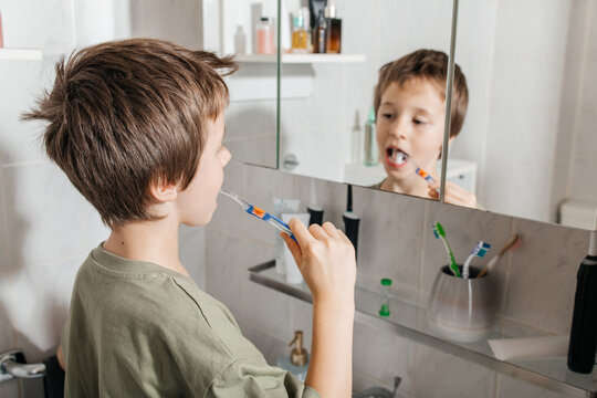 Boy brushing teeth with toothbrush in bathroom mirror during morning routine