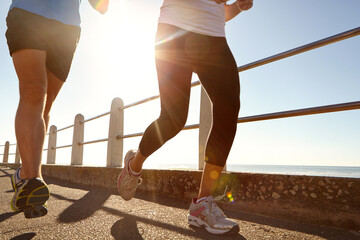 Boardwalk, running and legs of couple on beach for exercise, health or wellness together in morning. Fitness, sunshine and body of man with woman for cardio workout by ocean for training in summer.