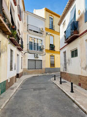 A quiet, cozy, narrow street in the city center on a sunny day. A street where residents live, with cute balconies and flowers hanging from the air-conditioned facade. Malaga, Spain, 2022. 