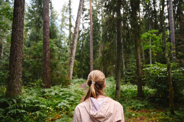 Person with hooded jacket standing in rainy summer forest back view