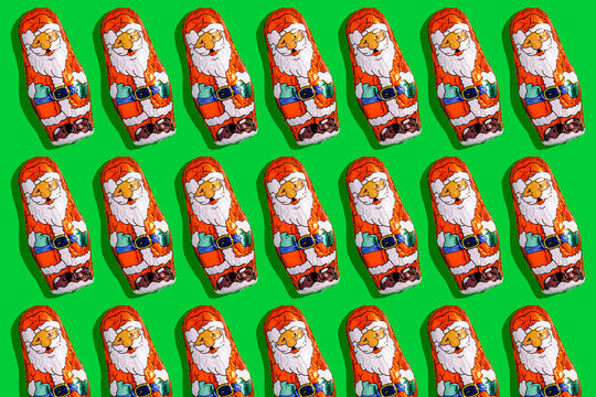 Mini Santa Claus chocolates in a festive pattern on green background