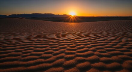 Golden sunset illuminates rippled sand dunes in a vast desert landscape with distant mountains
