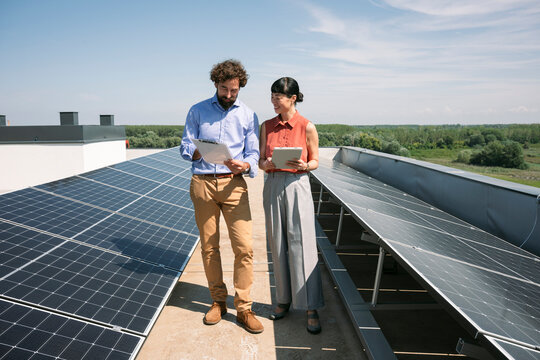 Business workers discussing renewable energy on rooftop with solar panels