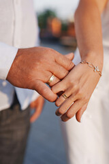 Couple holding hands with wedding rings in outdoor setting