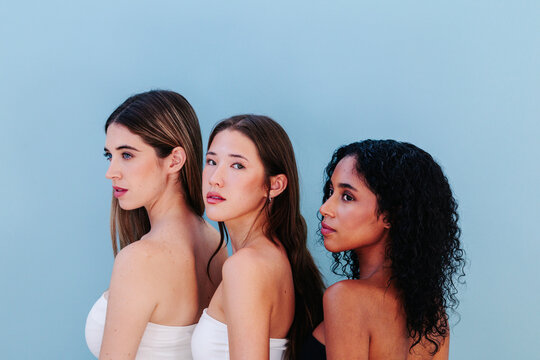 Three women standing in line with serious expressions against a minimalist background