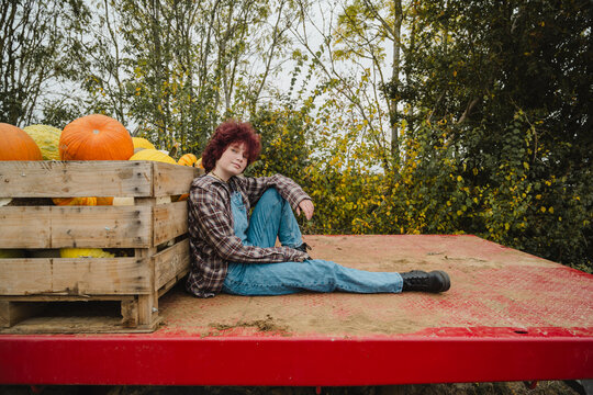 Teenager in dungarees sitting by pumpkins at outdoor pumpkin patch