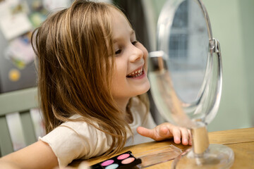 Smiling child playing with make-up at table in front of mirror