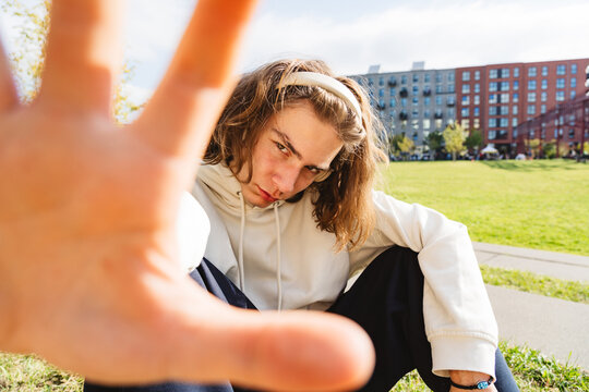Teenager showing stop gesture outdoors in urban park with defiant attitude