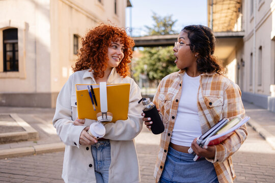 Two students walking and talking on campus holding books and coffee