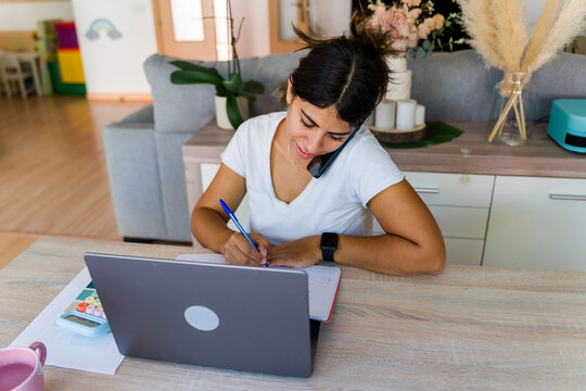 Woman multitasking in home office, focused on remote work and communication