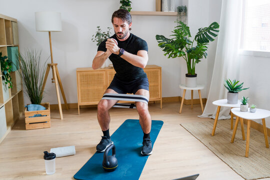Adult performing squat exercise with resistance band at home