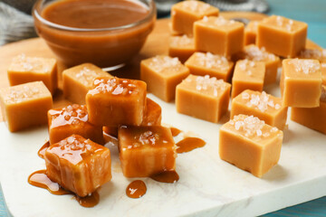 Tasty candies with salt and caramel sauce on light blue table, closeup