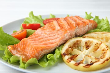 Piece of tasty grilled salmon, lemon slices and salad on white table, closeup