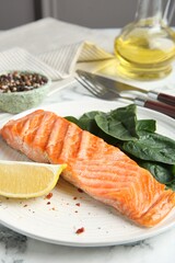 Piece of tasty grilled salmon, lemon slice and spinach served on white table, closeup