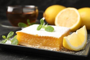 Tasty lemon bar with mint, fresh fruits and tea on black table, closeup
