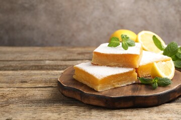 Tasty lemon bars with mint and fresh fruits on wooden table, closeup. Space for text