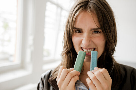 Playful woman biting chalk with energetic expression indoors