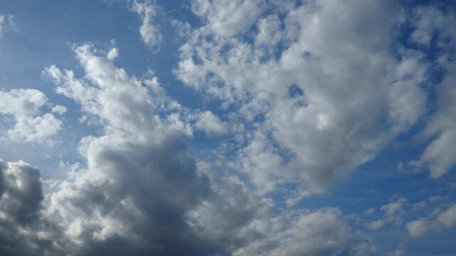 Time lapse of fluffy clouds which drift across bright blue sky as sunlight breaks through, creating a beautiful display of light and shadow. The scene captures nature beauty. Rapid quickly motion.