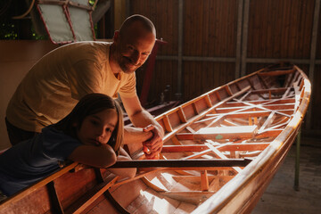 Father and son working on wooden boat together in sunny workshop