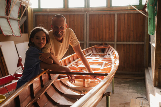 Father and son building a wooden boat together in a sunny workshop