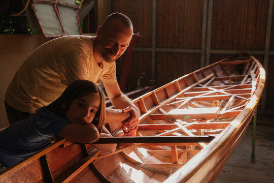 Father and son working on wooden boat together in sunny workshop
