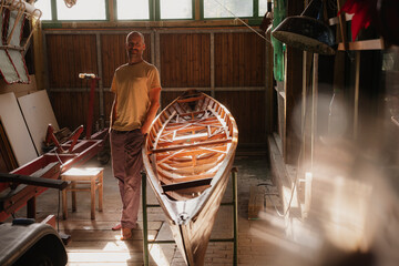 Man working on wooden boat in sunny workshop with tranquil atmosphere