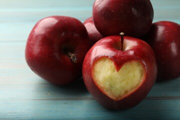 Red apple with carved heart and other fruits on blue wooden table, closeup