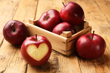 Red apple with carved heart and other fruits on wooden table, closeup