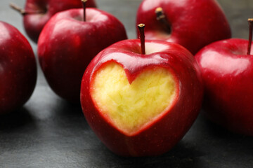 Red apple with carved heart and other fruits on black table, closeup