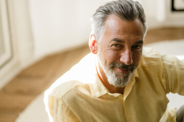 Smiling mature man with grey hair and beard relaxing at home
