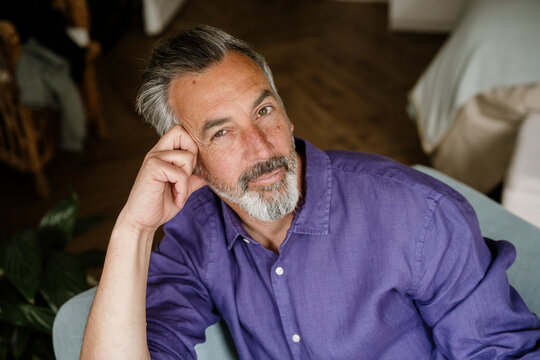 Portrait of a smart mature man in a purple shirt sitting at home