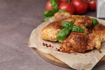 Tasty roasted chicken thighs with basil and tomatoes on grey table, closeup. Space for text