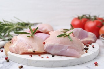 Raw chicken thighs with rosemary, peppercorns and tomatoes on white marble table, closeup