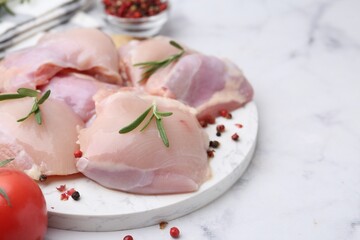 Raw chicken thighs with rosemary, peppercorns and tomato on white marble table, closeup. Space for text