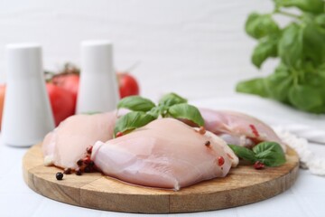 Raw chicken thighs with basil and peppercorns on white table, closeup
