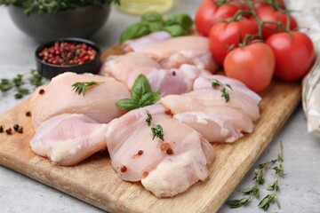 Raw chicken thighs with herbs, peppercorns and tomatoes on light table, closeup