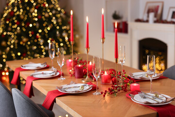 Stylish Christmas table setting with plates, glasses and burning candles in festive decorated room. Bokeh effect
