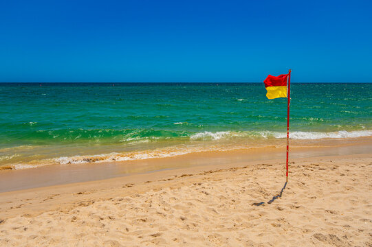 Red and yellow flag on sandy beach of Tavira Algarve Portugal