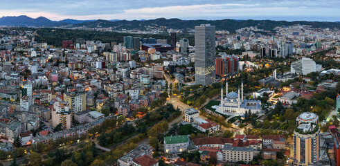 Obraz premium Dawn aerial panorama of central Tirana with modern towers, dense neighbourhoods and surrounding hills under soft morning light.