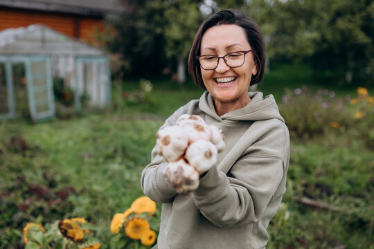 Smiling farmer holding fresh garlic outdoors in organic garden