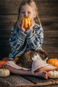 Child in rustic sweater holding pumpkin with rabbit and autumn decor