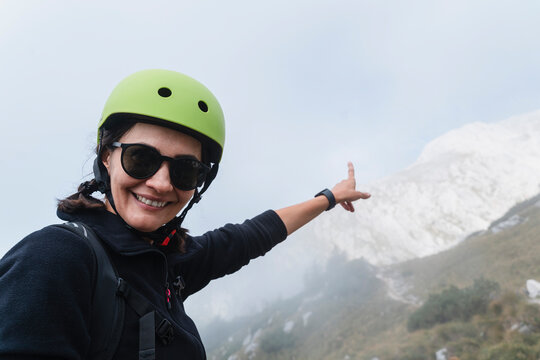 Smiling person with helmet points to mountain landscape outdoors