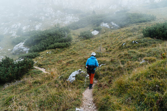 Hiker with backpack and helmet trekking on misty mountain trail