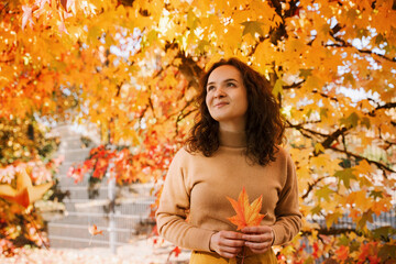 Curly haired woman outdoors holding autumn leaves in positive mood