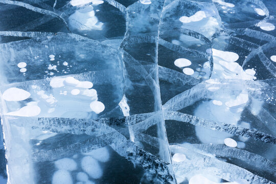 Beautiful natural winter ice texture with white bubbles and cracks in blue clear ice of frozen Baikal Lake in cold day. Abstract bright textured background. Top view, mock up, flat lay, close-up